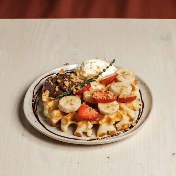 Waffles topped with chocolate, whipped cream, strawberries, bananas, and a sprig of thyme.