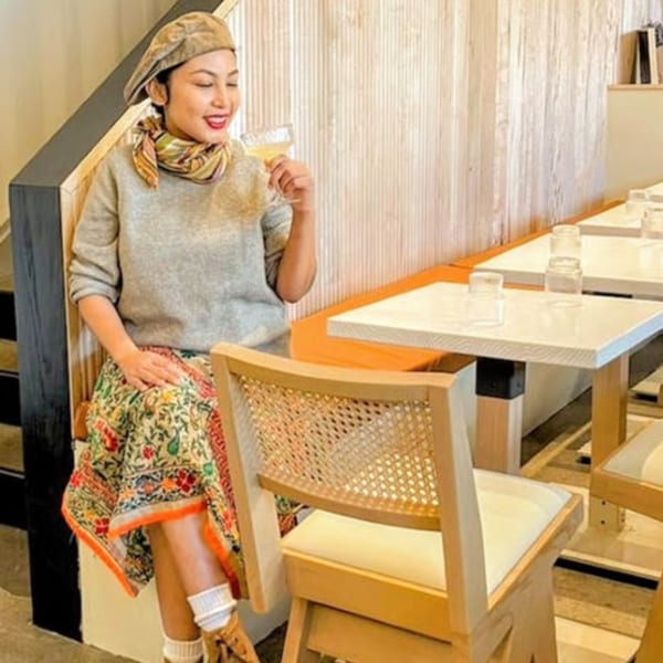 A woman in a Japandi bistro smiles while holding a drink, with light wood tables and chairs.