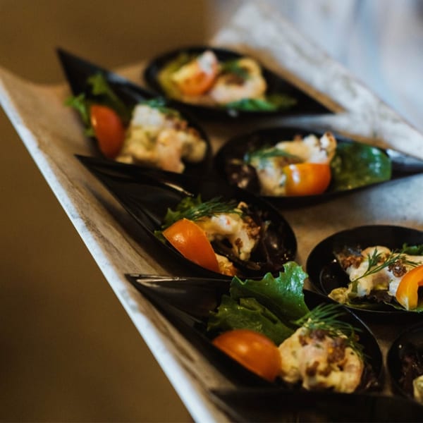 A tray of Japanese appetizers, each with lettuce, tomato, and a creamy topping in black spoons.