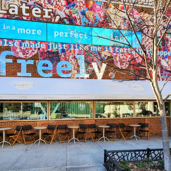 Nem's Japandi Bistro exterior with outdoor seating, a colorful mural, and a tree.