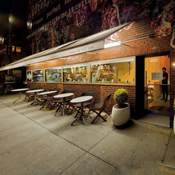 Nem's Japandi Bistro exterior at night with outdoor seating, a brick facade, and a person in the doorway.