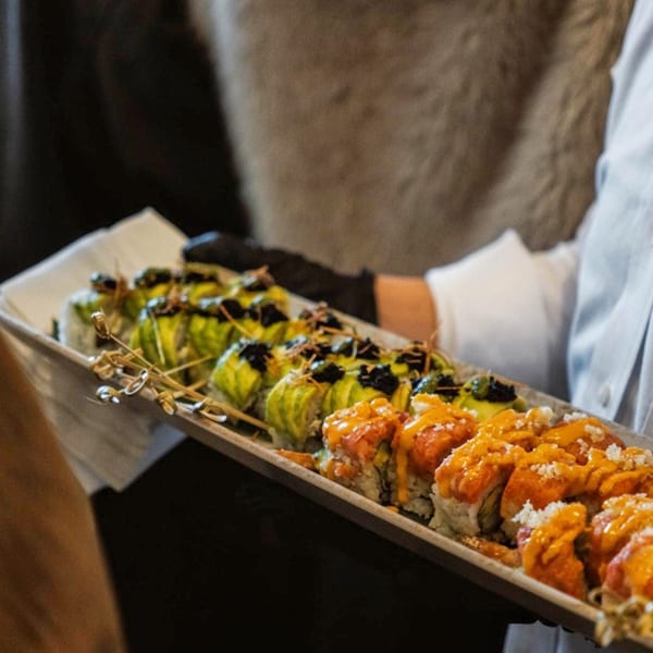 A server in black gloves carries a long tray of Nem's Japandi Bistro sushi rolls.