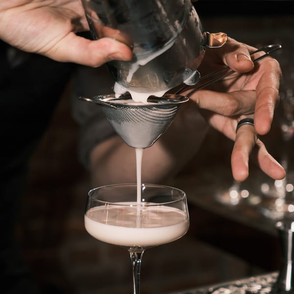 Bartender straining a creamy white cocktail from a shaker into a coupe glass at Nem's Japandi Bistro.