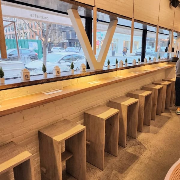 Interior of Nem's Japandi Bistro with a long window bar, wooden stools, and street view.