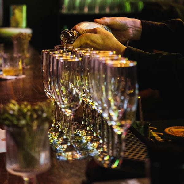 A bartender pours a drink into a row of glasses on a dark wooden bar at Nem's Japandi Bistro.