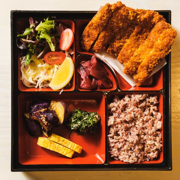 Overhead view of a Nem's Japandi Bistro bento box with tonkatsu, rice, salad, and sides.